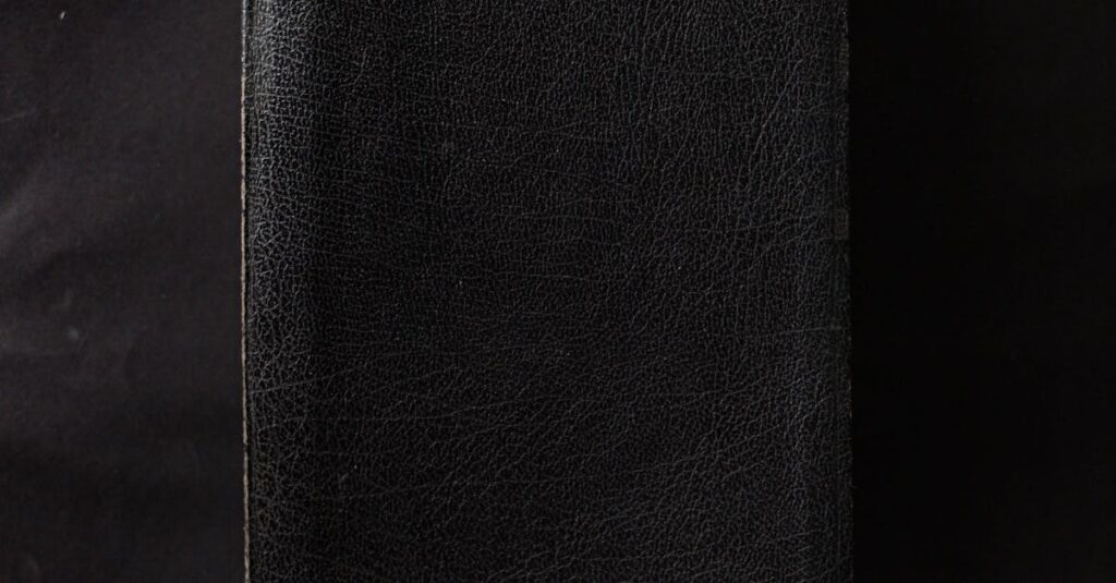 A closed black leather-bound book on a plain black surface.